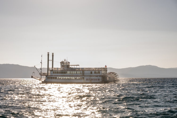M.S. Dixie II paddlewheel boat cruises on Lake Tahoe, illuminated by sunlight with mountain silhouettes in the background.