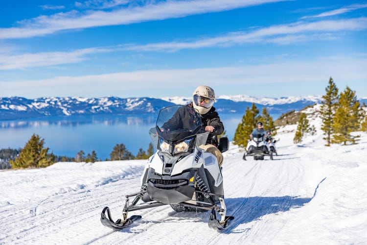 man in a red jacket on a snowmobile with mountains in the background