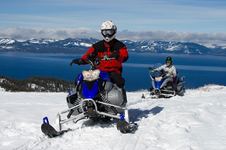 man in a red jacket on a snowmobile with mountains in the background